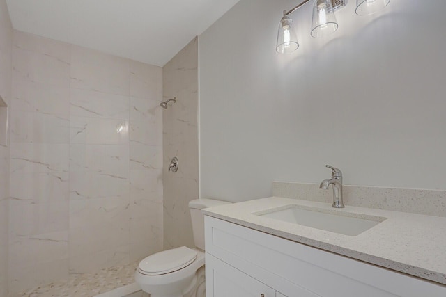 bathroom featuring a tile shower, vanity, and toilet