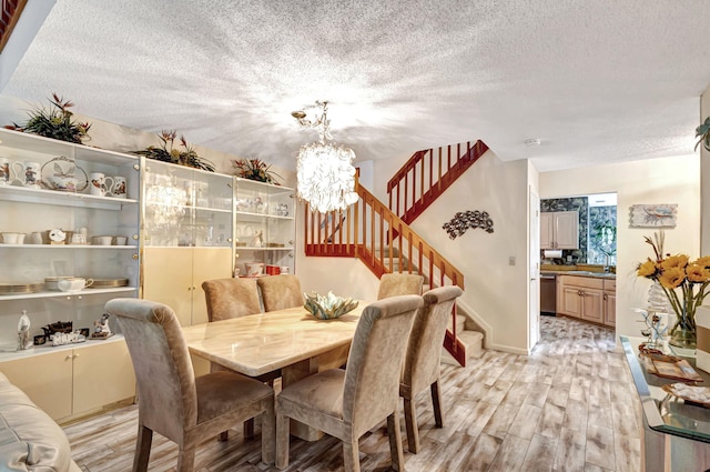 dining area with a textured ceiling, light wood-type flooring, and an inviting chandelier