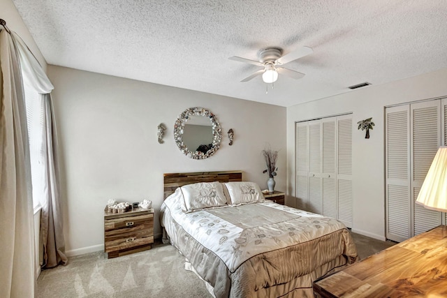 carpeted bedroom featuring a textured ceiling, ceiling fan, and multiple closets