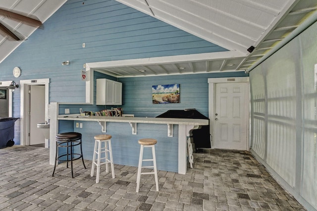 exterior space featuring kitchen peninsula, a breakfast bar, vaulted ceiling, wooden walls, and white cabinets