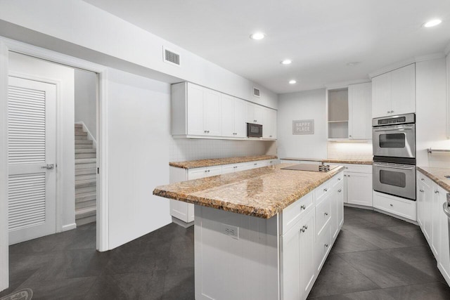 kitchen with a center island, backsplash, black appliances, light stone counters, and white cabinetry