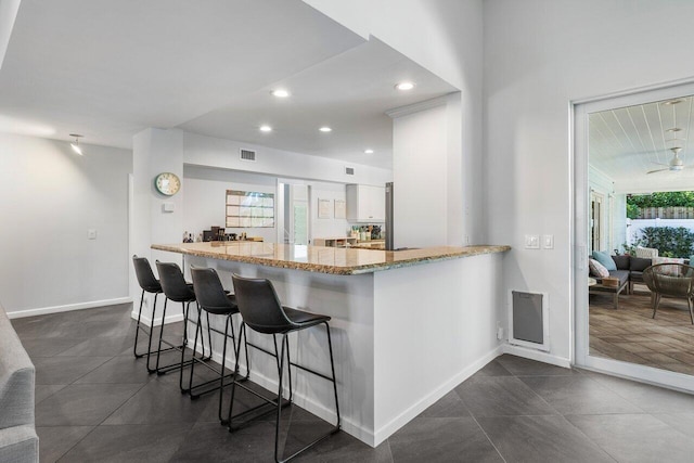 kitchen featuring white cabinets, ceiling fan, light stone countertops, kitchen peninsula, and a breakfast bar area