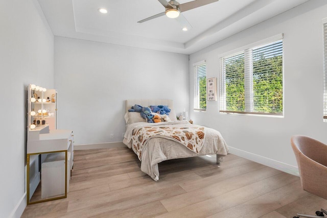 bedroom with ceiling fan, a raised ceiling, and light hardwood / wood-style flooring