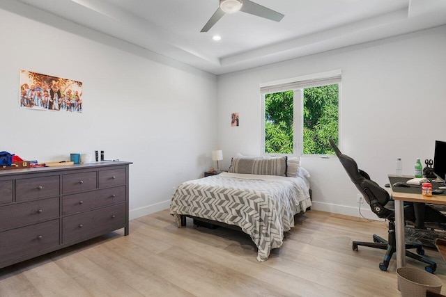 bedroom featuring light hardwood / wood-style floors, a raised ceiling, and ceiling fan