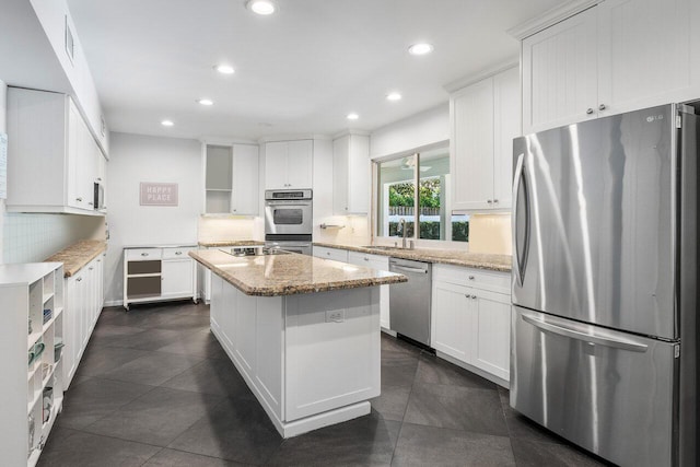 kitchen with light stone countertops, appliances with stainless steel finishes, backsplash, a center island, and white cabinetry