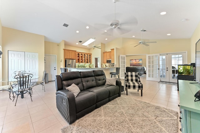 tiled living room with ceiling fan, a skylight, high vaulted ceiling, and french doors