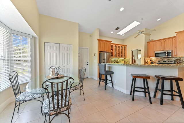 kitchen featuring decorative backsplash, light stone countertops, stainless steel appliances, and a skylight