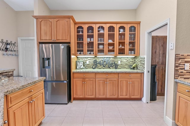 kitchen with light tile patterned flooring, light stone countertops, stainless steel refrigerator with ice dispenser, and tasteful backsplash