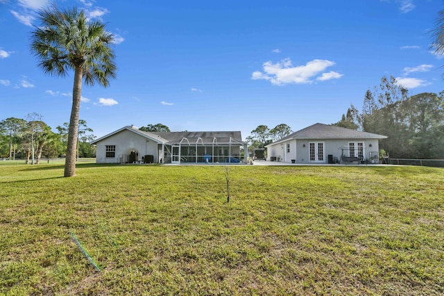 rear view of house with french doors, a yard, and a lanai