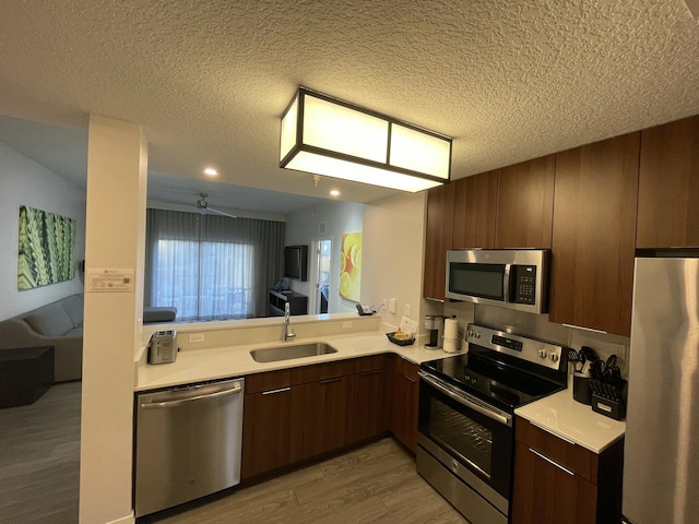 kitchen featuring appliances with stainless steel finishes, light wood-type flooring, a textured ceiling, ceiling fan, and sink