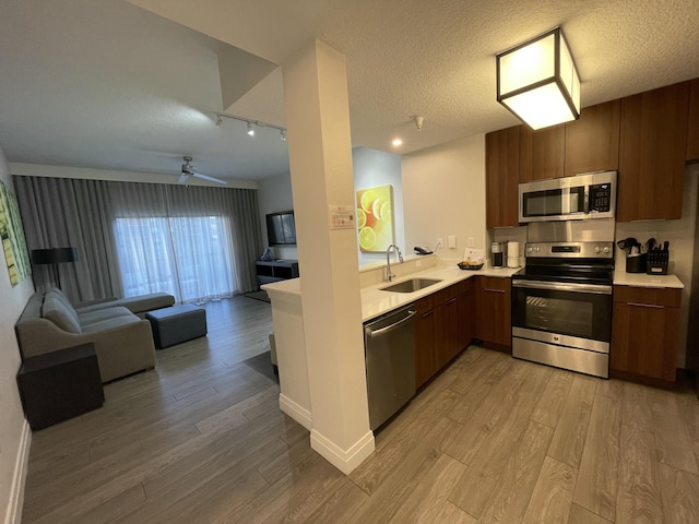 kitchen with light wood-type flooring, a textured ceiling, stainless steel appliances, ceiling fan, and sink