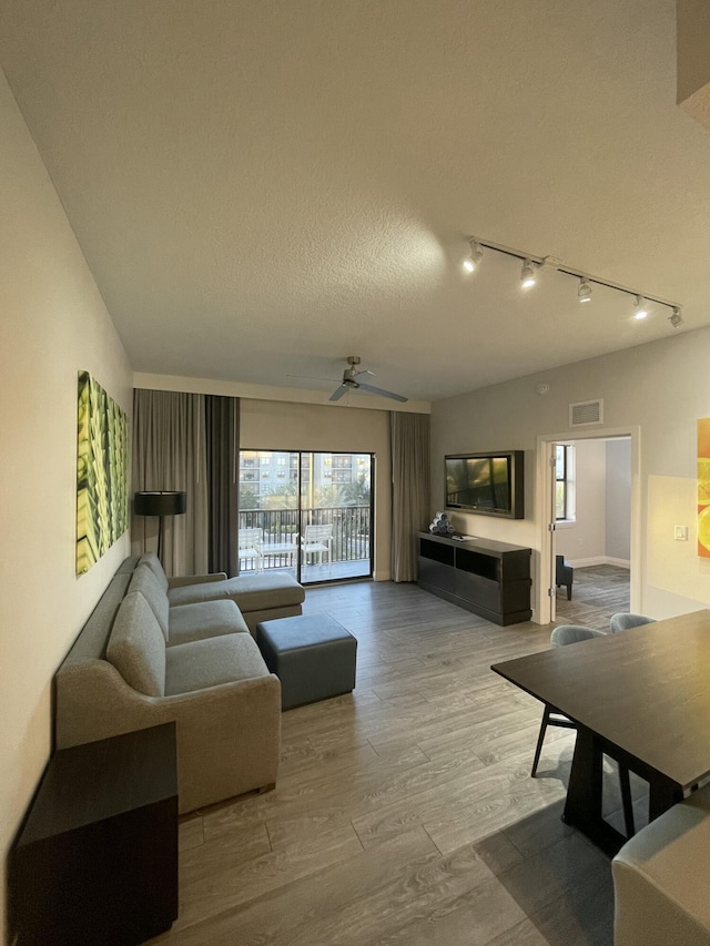 living room with ceiling fan, rail lighting, wood-type flooring, and a textured ceiling