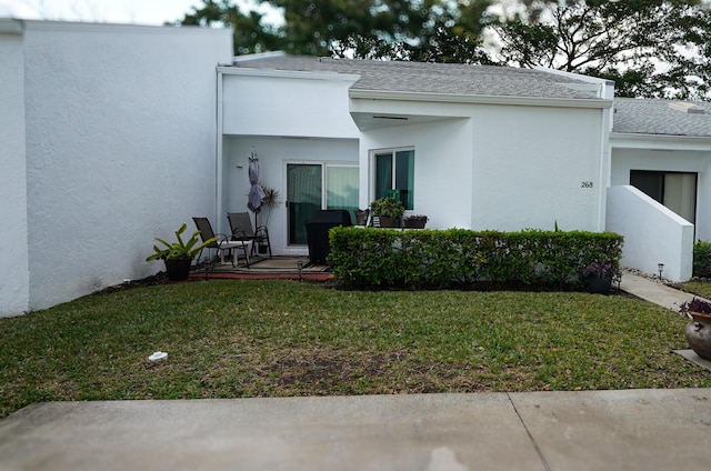 back of property featuring a shingled roof, a lawn, and stucco siding