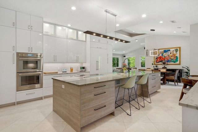 kitchen featuring double oven, white cabinets, a spacious island, and vaulted ceiling