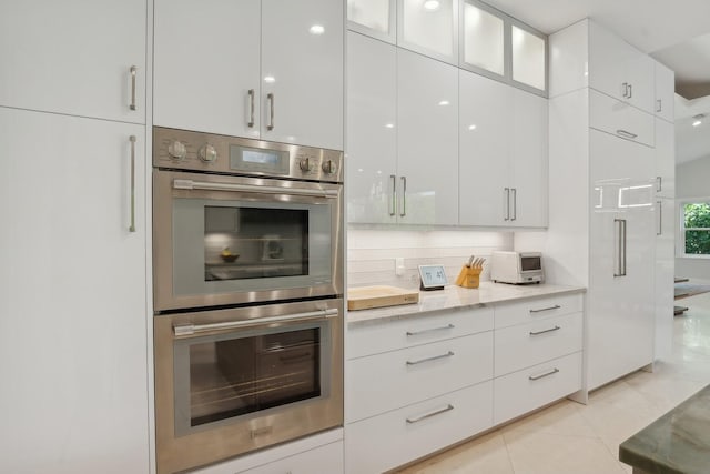 kitchen featuring double oven, white cabinetry, light tile patterned flooring, and decorative backsplash