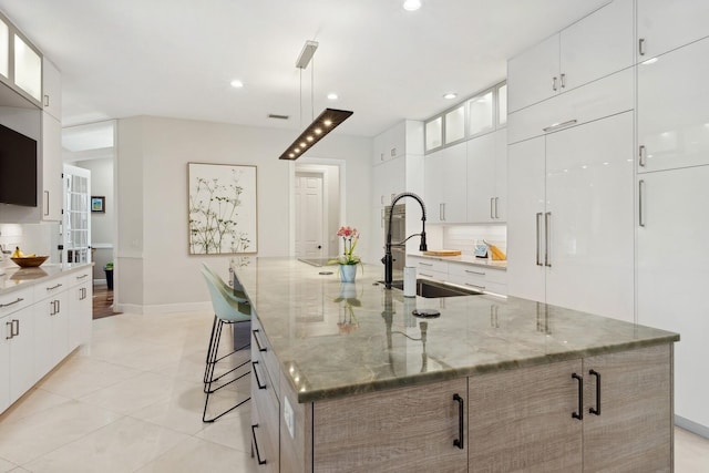 kitchen with light stone countertops, a spacious island, white cabinetry, a kitchen breakfast bar, and sink