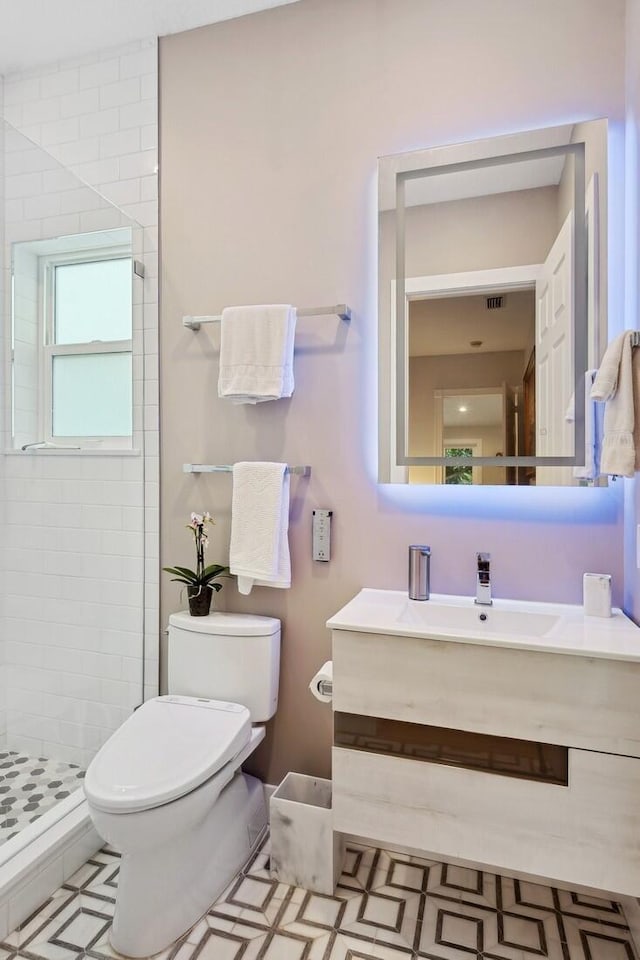 bathroom with toilet, a tile shower, and vanity