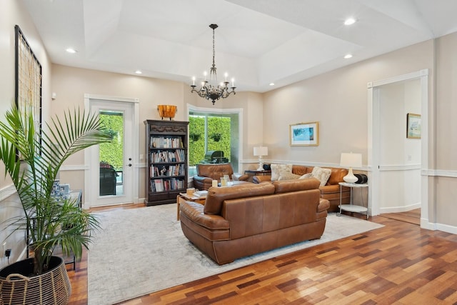 living room featuring a raised ceiling, wood-type flooring, and a chandelier