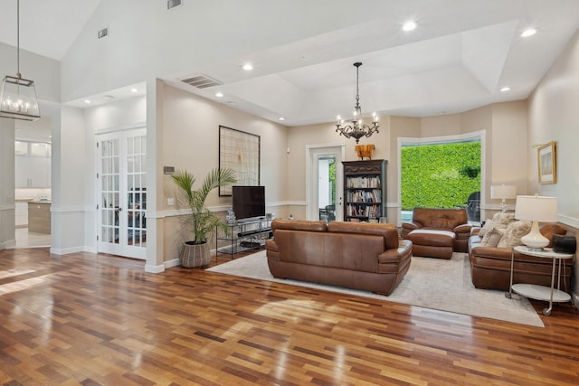 living room with a towering ceiling, a chandelier, hardwood / wood-style floors, and a tray ceiling