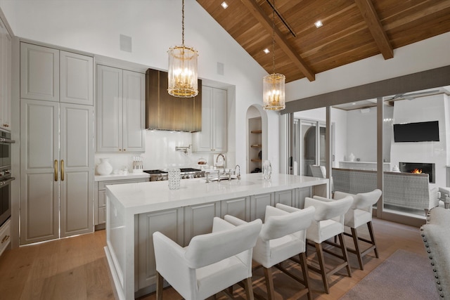 kitchen with wood ceiling, a center island with sink, high vaulted ceiling, beamed ceiling, and a fireplace