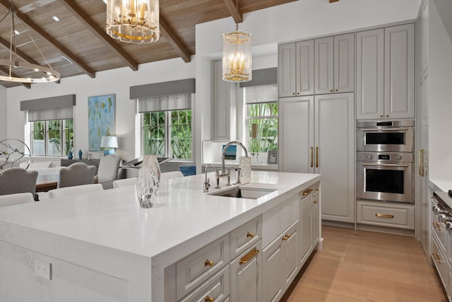 kitchen with gray cabinetry, sink, a notable chandelier, pendant lighting, and a kitchen island with sink