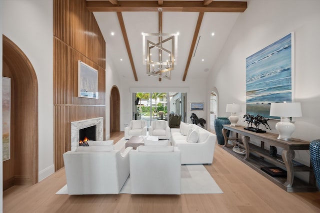 living room featuring light wood-type flooring, beam ceiling, high vaulted ceiling, a premium fireplace, and a chandelier