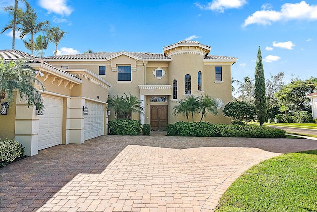 mediterranean / spanish-style house featuring an attached garage, a tiled roof, decorative driveway, and stucco siding