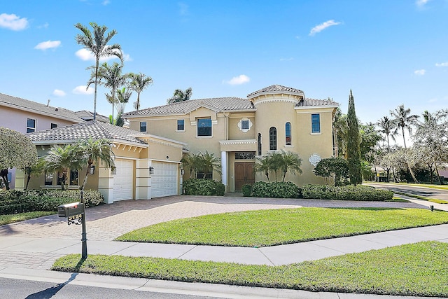 mediterranean / spanish house featuring a front yard, decorative driveway, a tiled roof, and stucco siding