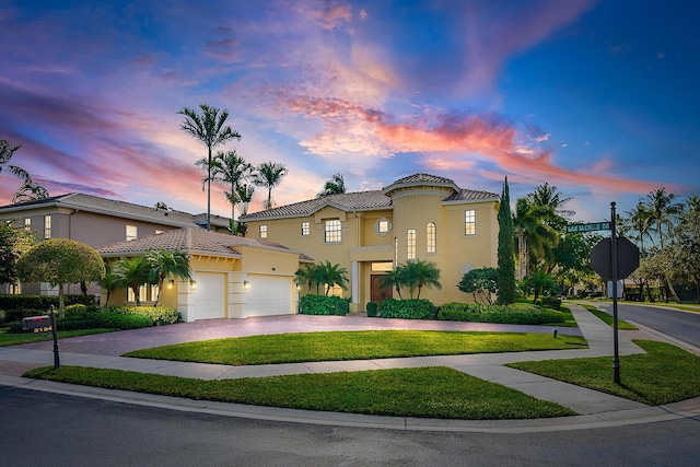 mediterranean / spanish-style home with driveway, stucco siding, a tiled roof, an attached garage, and a front yard