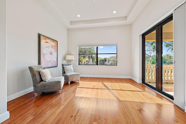 sitting room with light wood-style floors, a tray ceiling, and baseboards