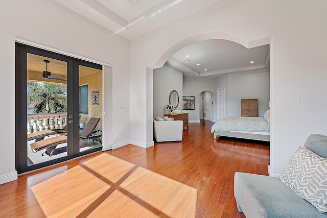 bedroom with arched walkways, wood finished floors, access to exterior, french doors, and a tray ceiling