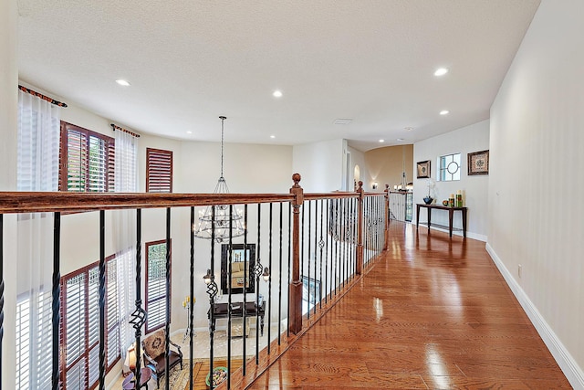 hall with a textured ceiling, recessed lighting, wood finished floors, baseboards, and an inviting chandelier