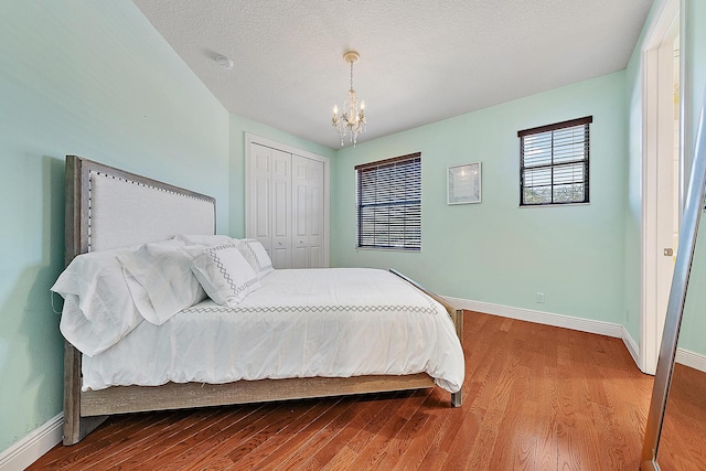 bedroom with a closet, baseboards, wood finished floors, a textured ceiling, and a notable chandelier