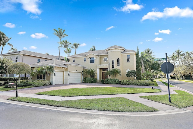 mediterranean / spanish house featuring decorative driveway, a tile roof, stucco siding, an attached garage, and a front lawn