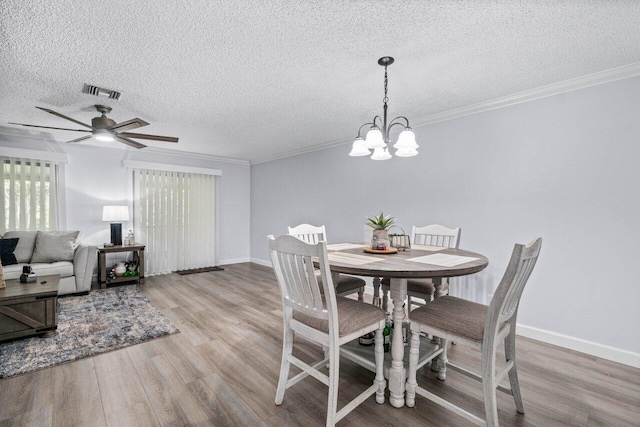 dining space with ceiling fan with notable chandelier, a textured ceiling, ornamental molding, and light hardwood / wood-style flooring