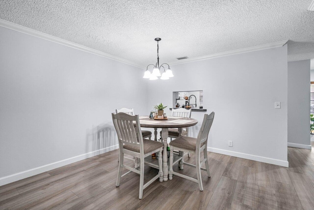 dining area with a notable chandelier, light hardwood / wood-style floors, ornamental molding, and a textured ceiling