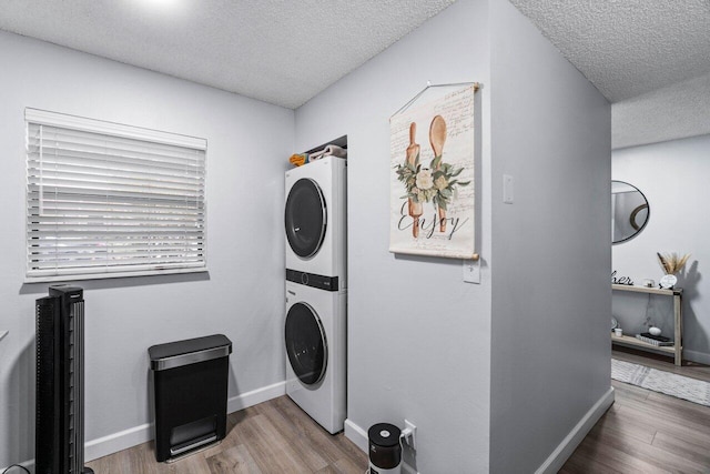 laundry area with a textured ceiling, stacked washing maching and dryer, and wood-type flooring