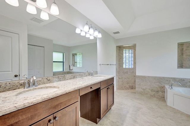 bathroom with a tray ceiling, a bathing tub, vanity, and tile walls