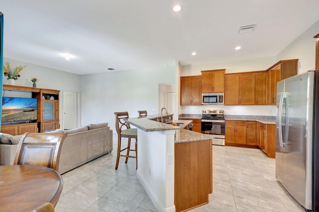 kitchen featuring a kitchen bar, light stone countertops, stainless steel appliances, a kitchen island with sink, and sink