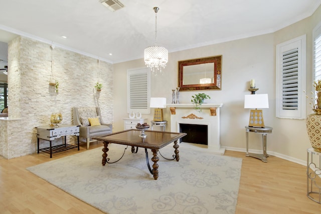 living area featuring visible vents, a fireplace with raised hearth, ornamental molding, wood finished floors, and an inviting chandelier