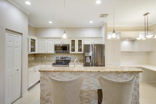 kitchen with decorative light fixtures, white cabinetry, appliances with stainless steel finishes, an island with sink, and glass insert cabinets