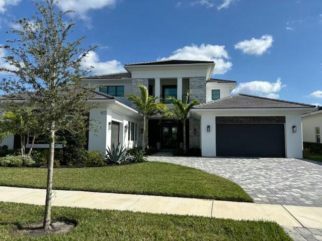 prairie-style house with a garage, decorative driveway, a front lawn, and stucco siding