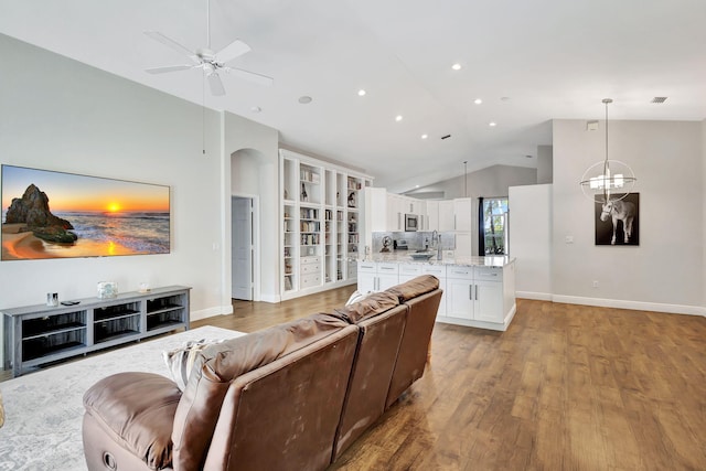 living room with sink, ceiling fan with notable chandelier, light hardwood / wood-style floors, and lofted ceiling