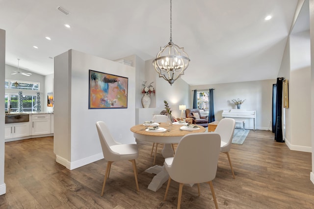 dining space with dark hardwood / wood-style flooring, ceiling fan with notable chandelier, and vaulted ceiling