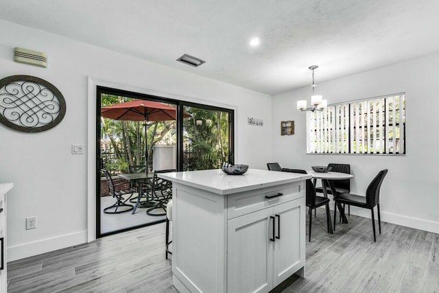 kitchen with white cabinets, pendant lighting, a kitchen island, and light hardwood / wood-style floors