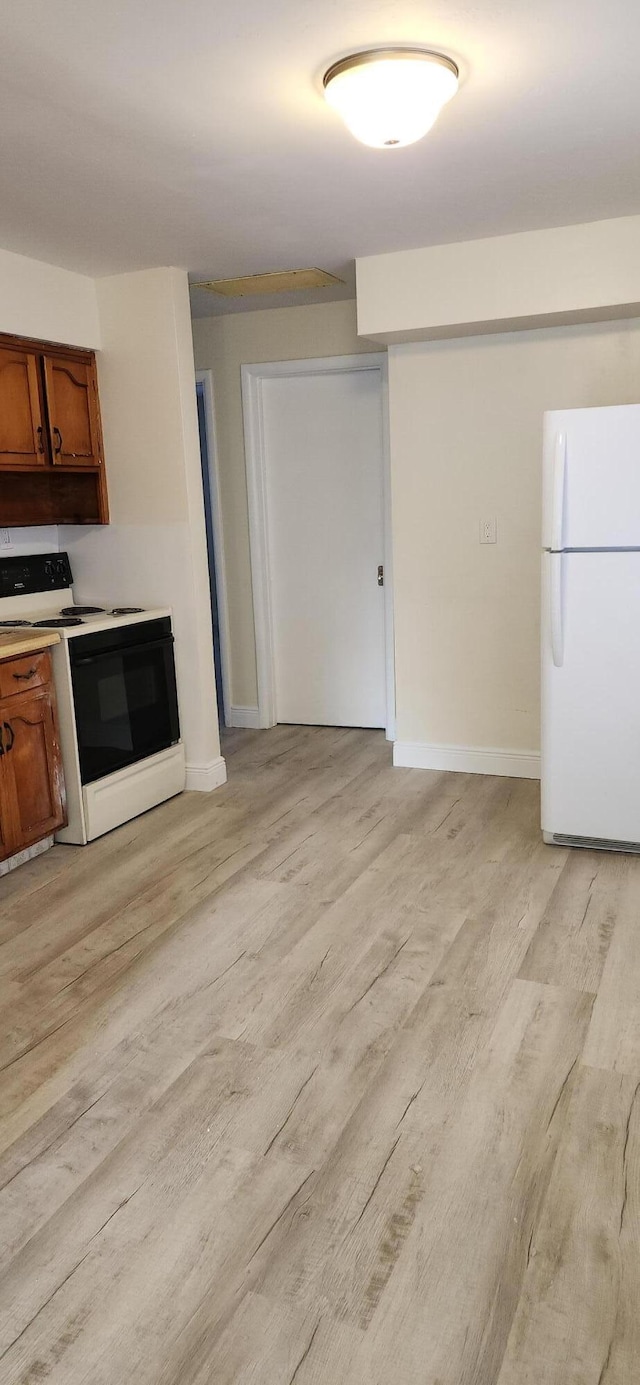 kitchen featuring light wood finished floors, light countertops, brown cabinetry, freestanding refrigerator, and range with electric cooktop