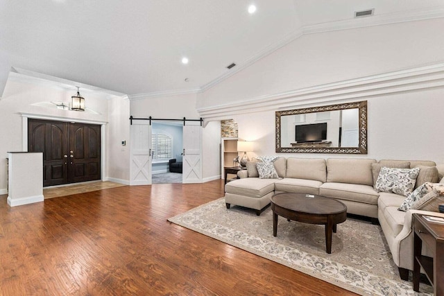 living room with a barn door, hardwood / wood-style flooring, vaulted ceiling, and ornamental molding