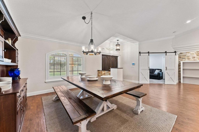 dining area with a barn door, hardwood / wood-style floors, a chandelier, vaulted ceiling, and ornamental molding