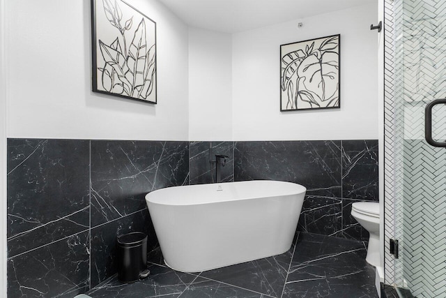 bathroom with a washtub, toilet, and tile walls