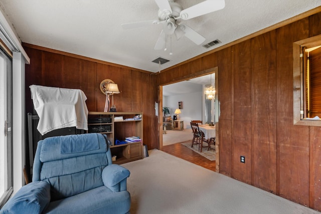 living area featuring ceiling fan, carpet, wood walls, and a textured ceiling